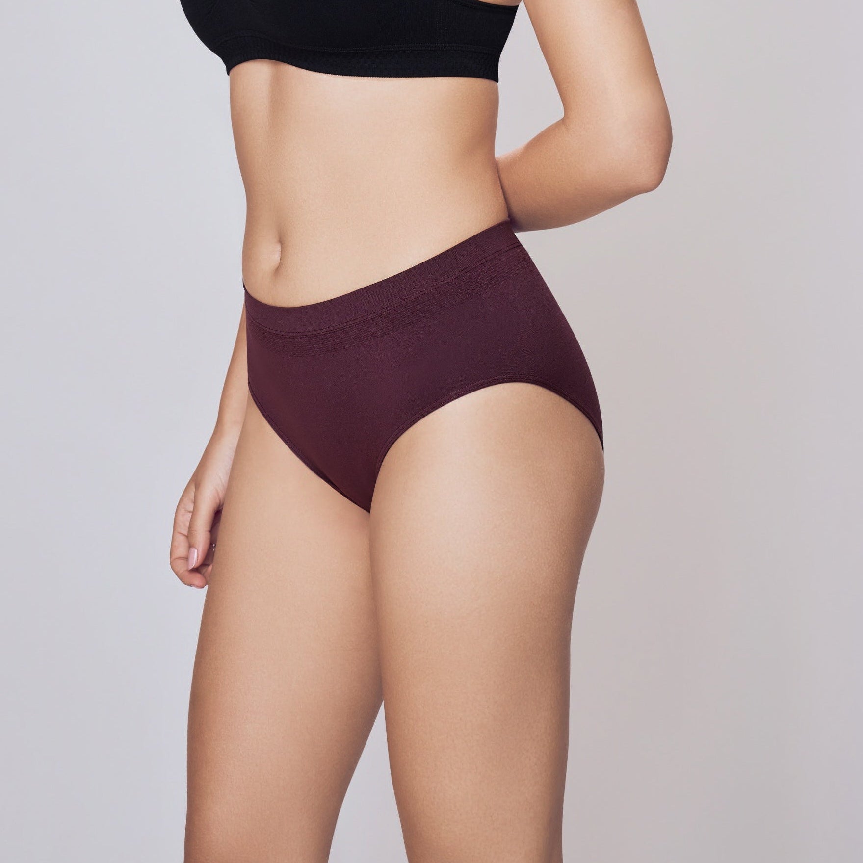 Woman wearing a black sports bra and maroon Lady Care Air V Hipster Panty underwear on a gray background