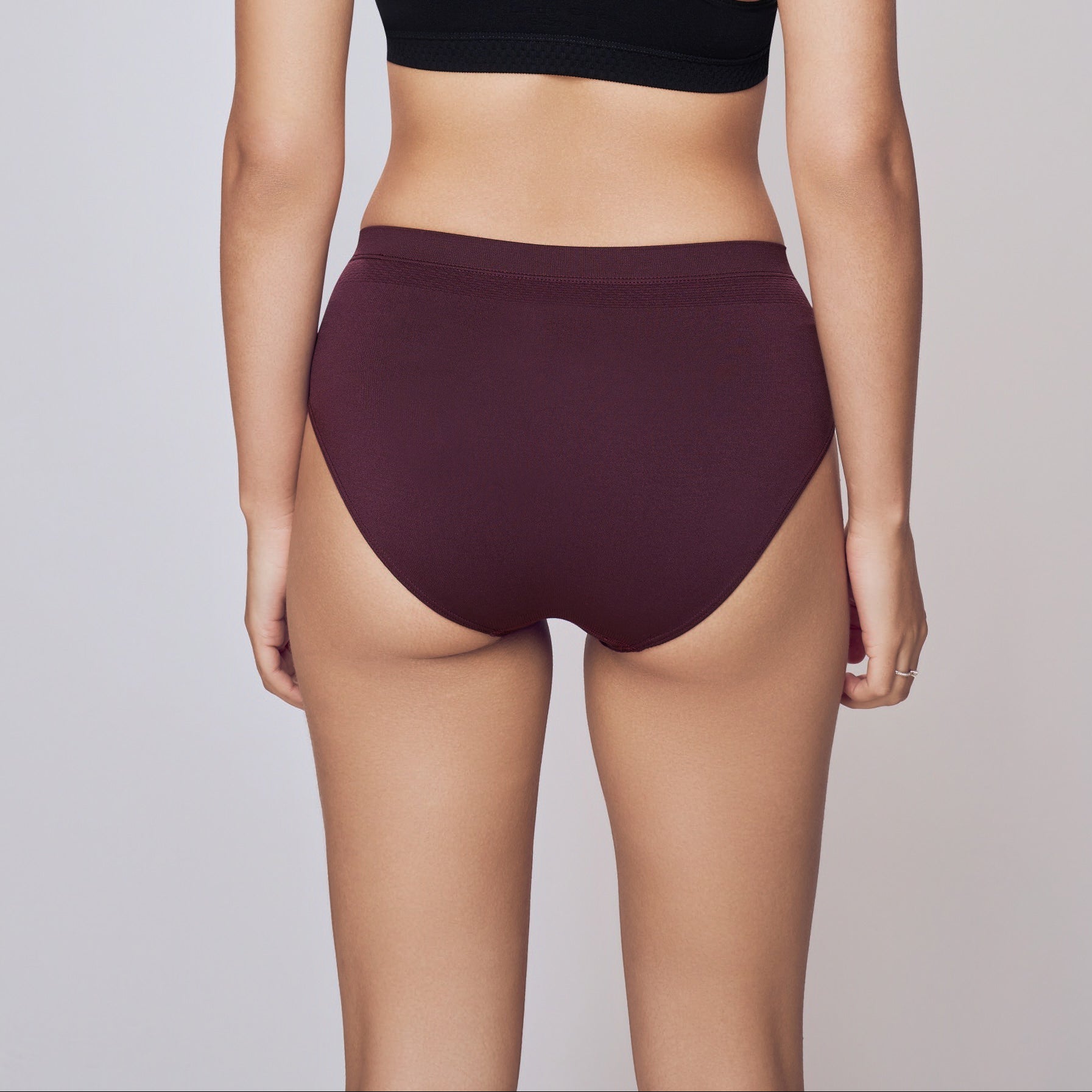 Woman wearing a black sports bra and maroon high-waisted shorts on a gray background