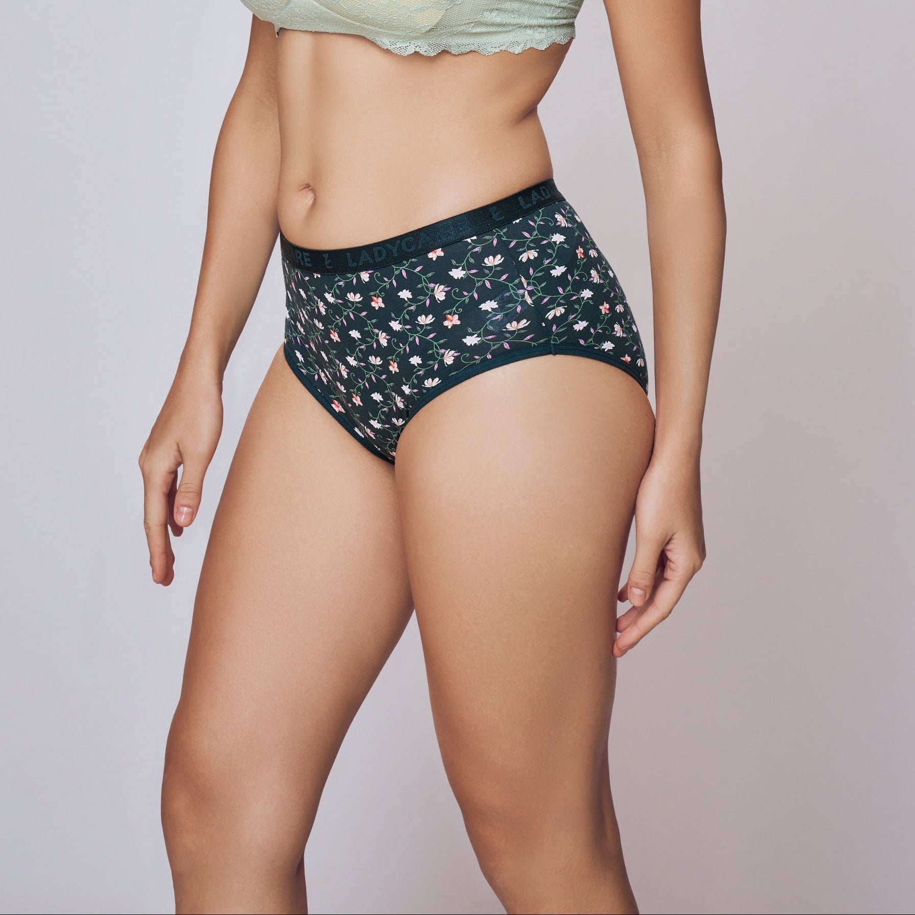 Woman wearing a light green strapless top and dark patterned shorts on a plain background
