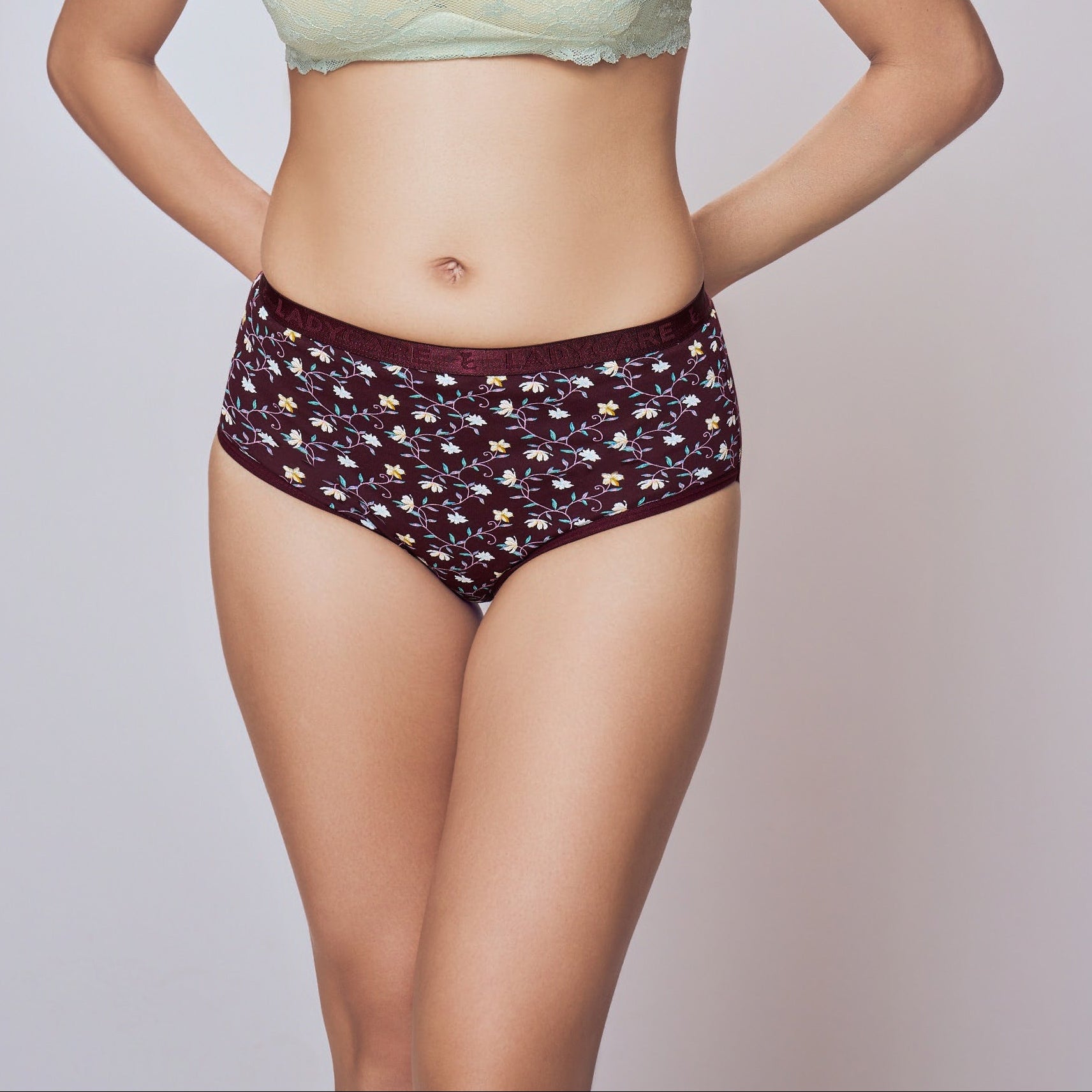 Woman wearing a light green bikini top and dark patterned bottoms on a plain background