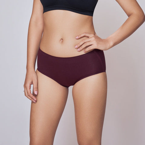Woman wearing a black sports bra and maroon Lady Care Think Hipster Panty on a gray background