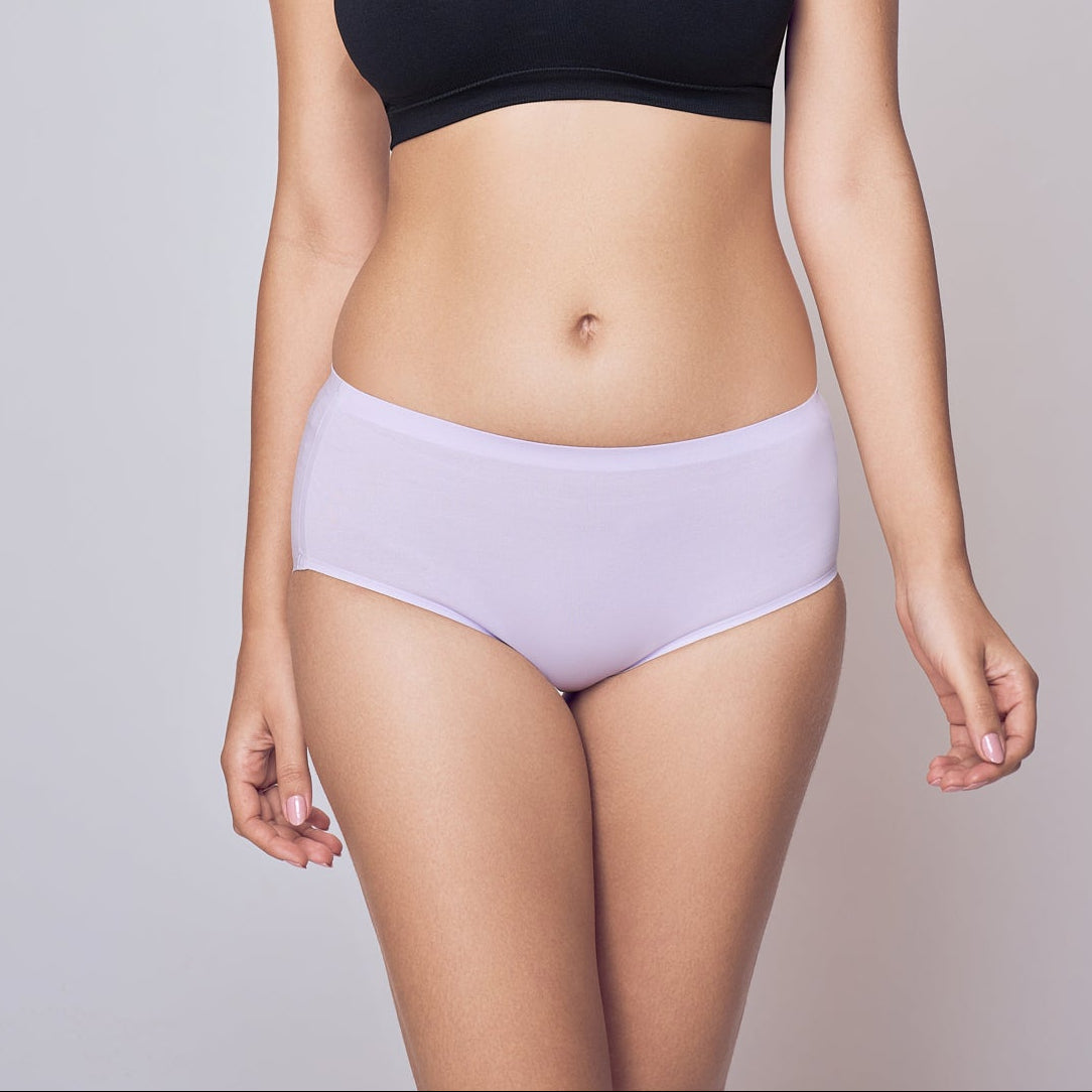 Woman wearing a black sports bra and light purple Lady Care Think Hipster Panty on a gray background