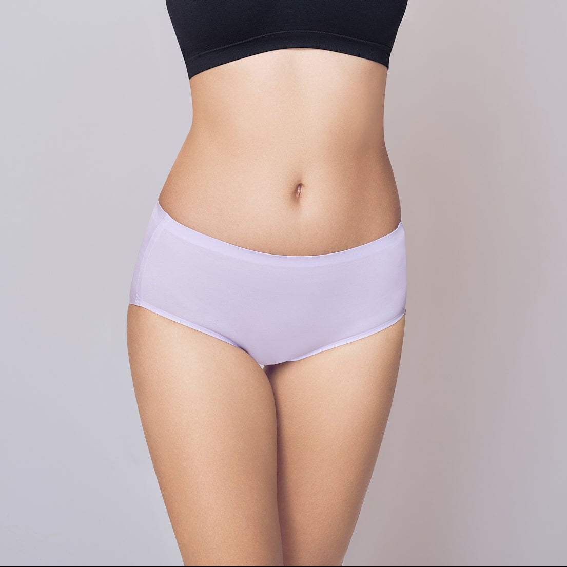 Woman wearing a black sports bra and light purple Lady Care Think Hipster Panty on a gray background