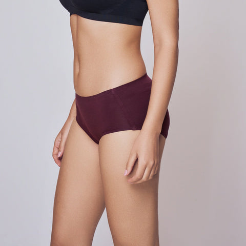 Woman wearing a black bikini top and maroon Lady Care Think Hipster Panty on a gray background