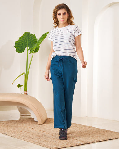 Woman wearing a white striped shirt and blue pants standing in a minimalistic room with a plant.