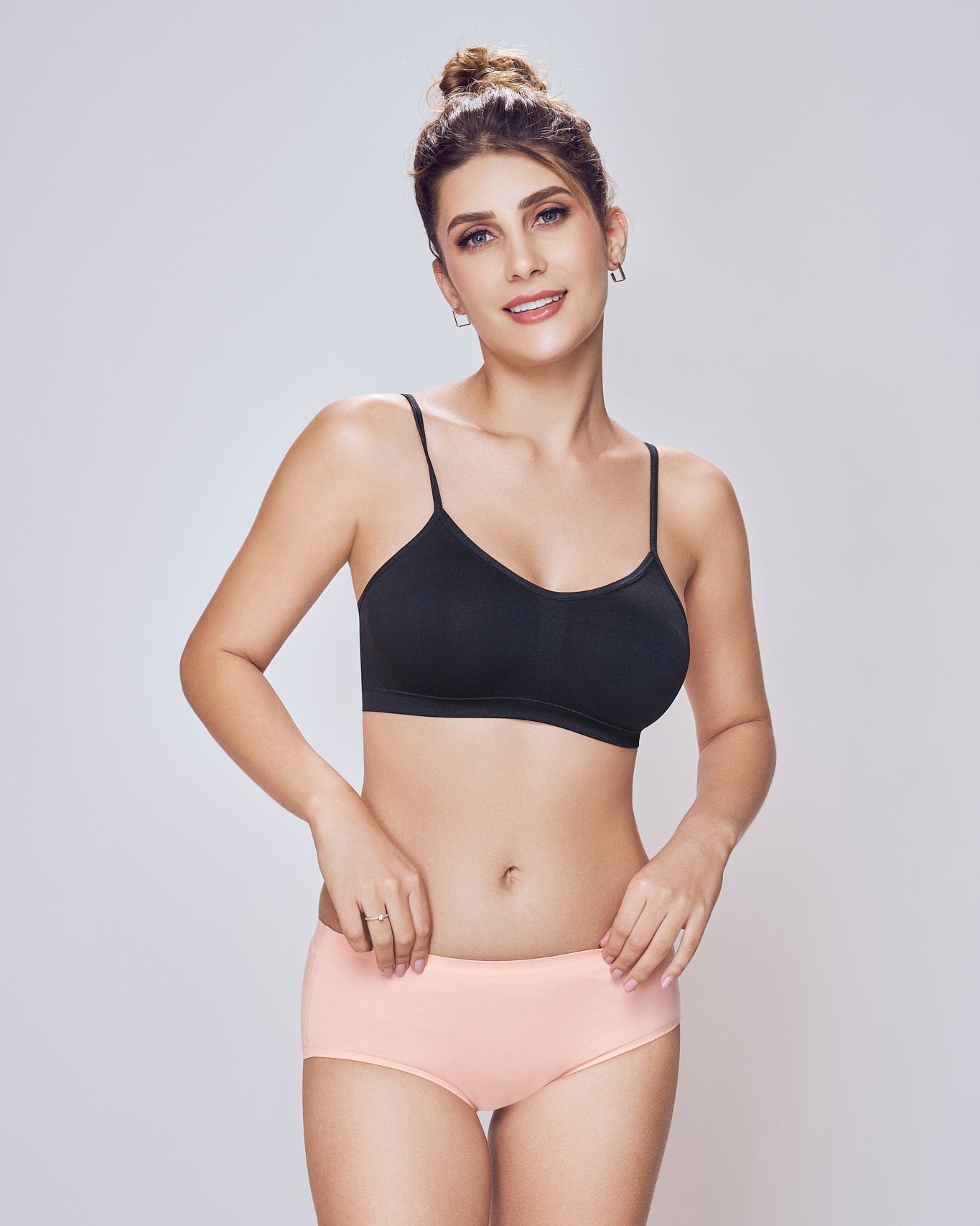 Woman wearing a black bra and pink underwear on a light gray background
