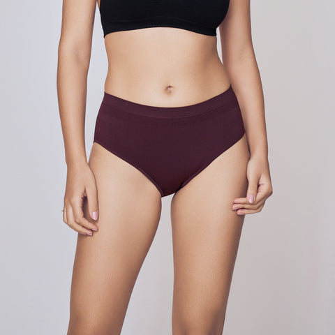 Woman wearing a black sports bra and maroon high-waisted underwear on a gray background