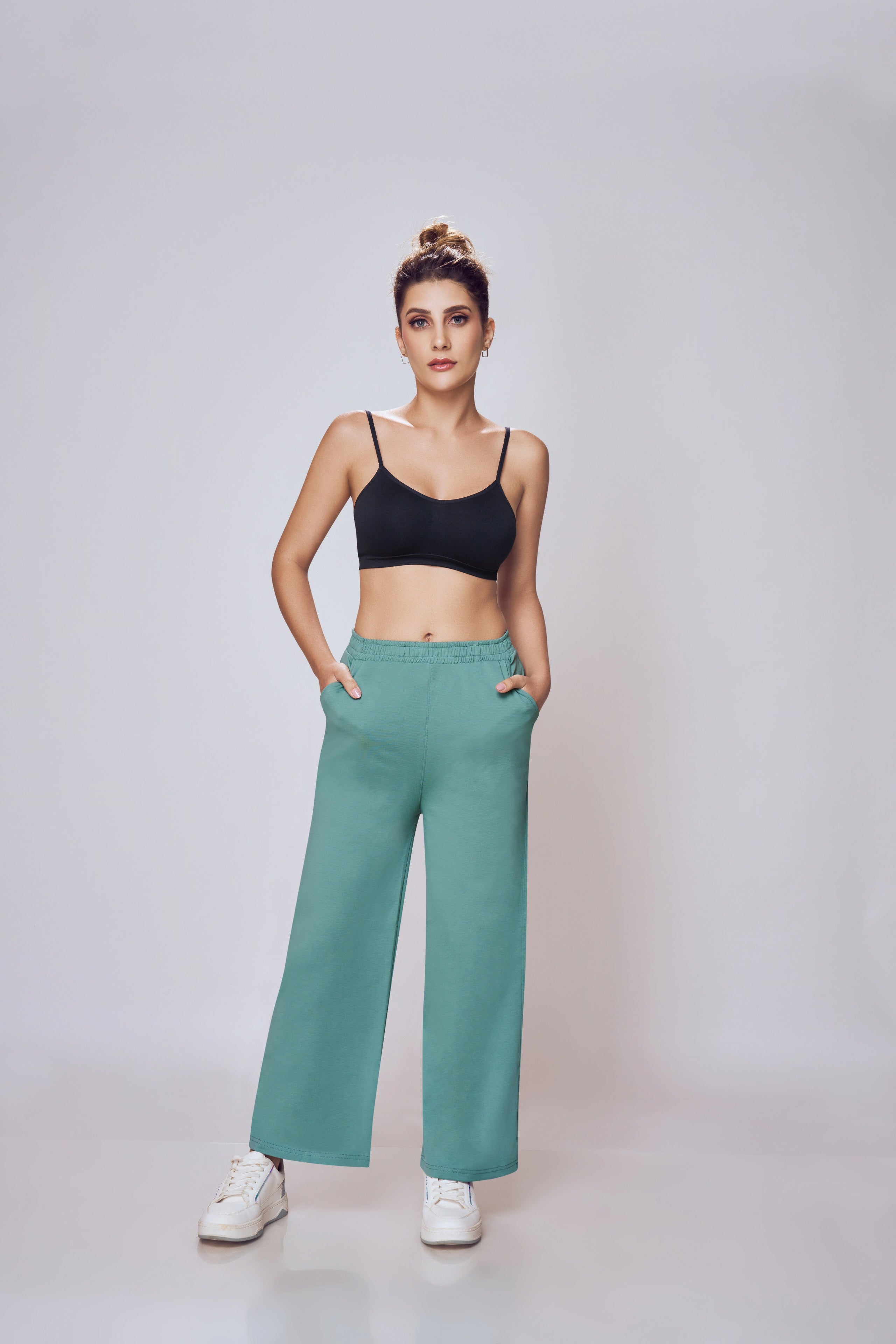 Woman wearing a black sports bra and teal pants on a plain background