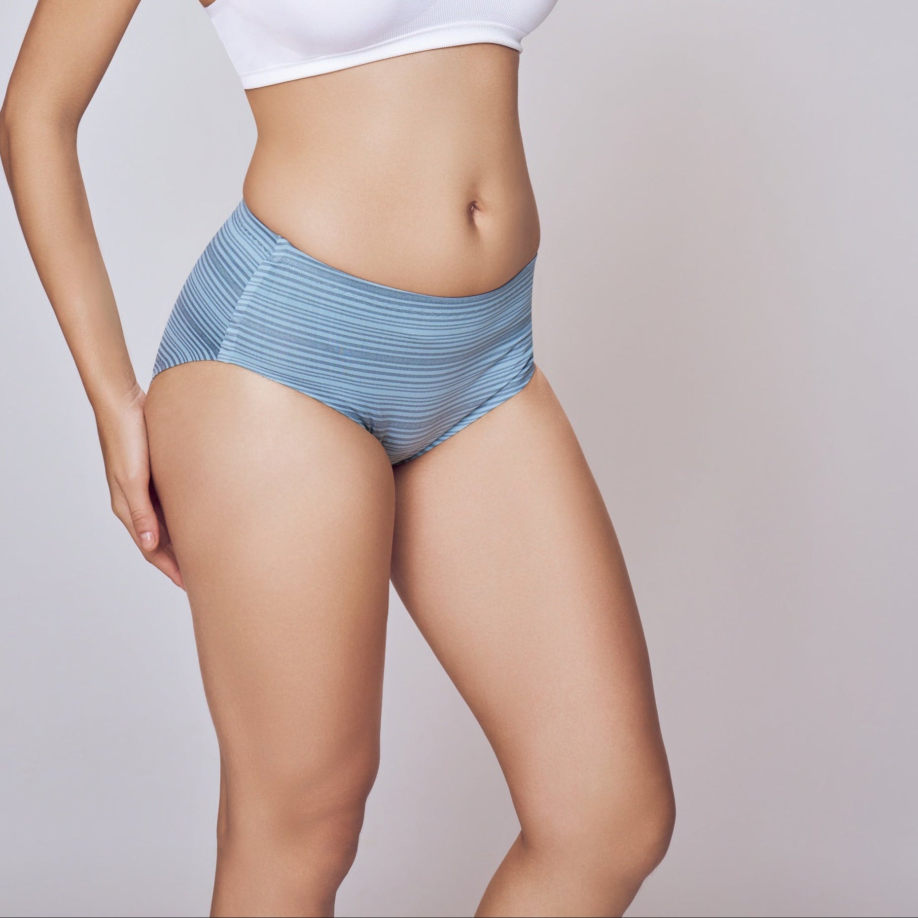 Woman wearing a white sports bra and blue underwear on a plain background