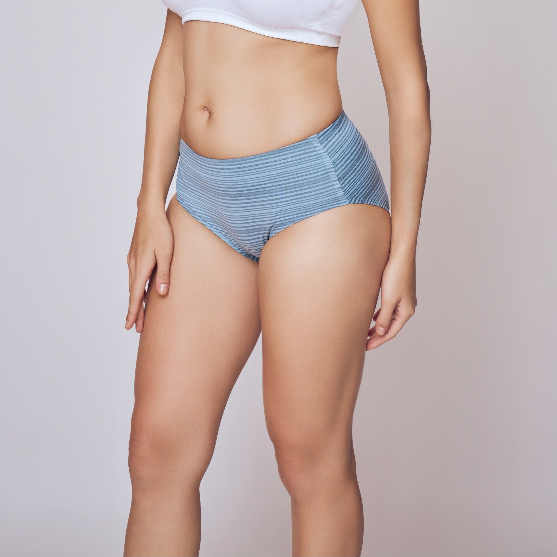 Woman wearing a white tank top and blue underwear on a plain background