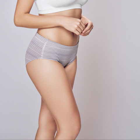 Woman wearing a white bra and gray underwear on a plain background