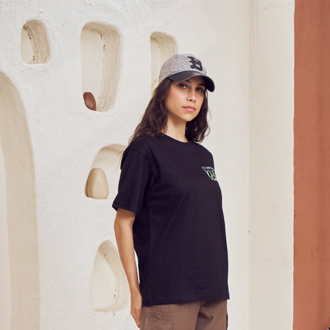 Person wearing a black t-shirt and brown pants standing in front of a textured wall.