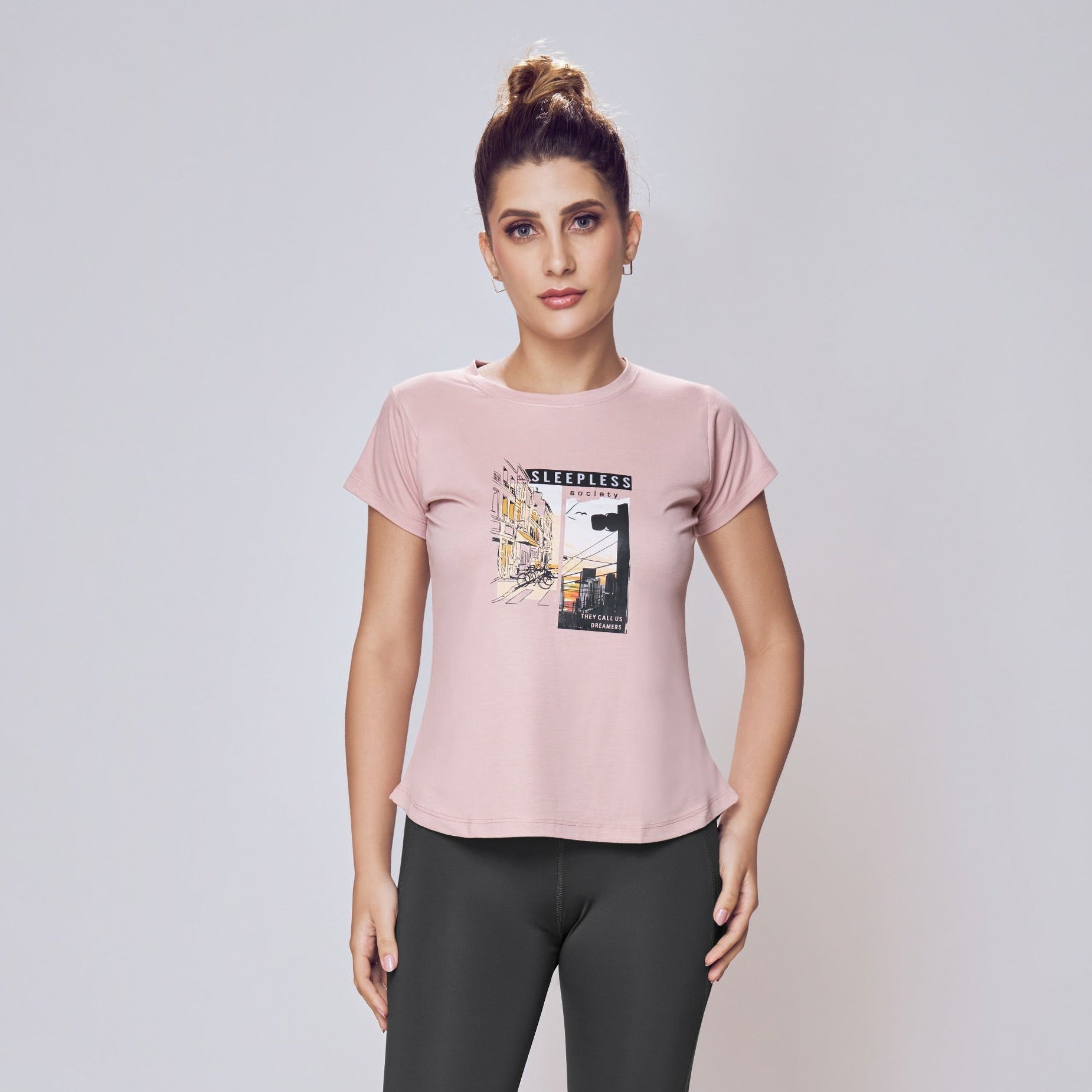 Woman wearing a pink t-shirt with a graphic design and black leggings on a white background