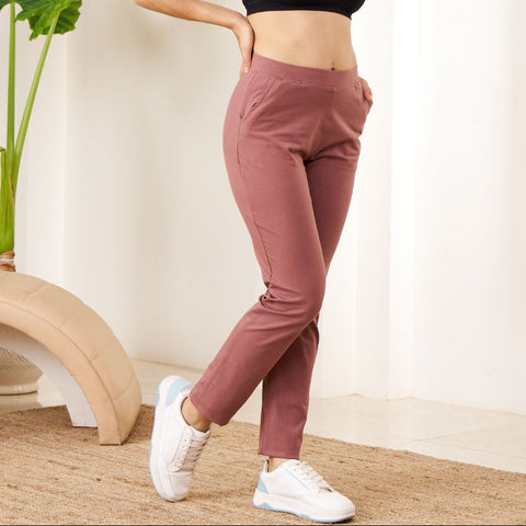 Woman in black sports bra and pink Power Move Track Pants posing in a room with a plant and white wall.