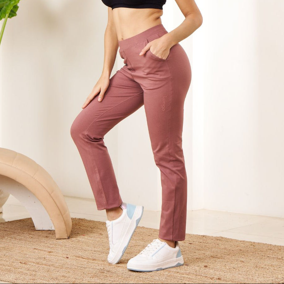 Woman in black sports bra and pink Power Move Track Pants posing in a minimalistic room.