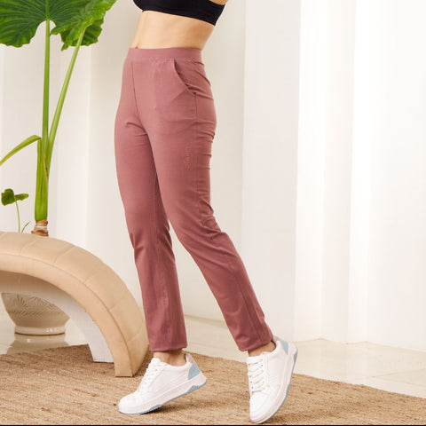 Woman in black sports bra and pink Power Move Track Pants standing indoors with a plant in the background