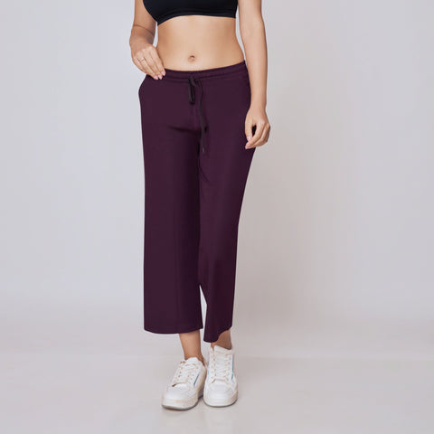 Woman wearing a black sports bra and purple Ankle Length Track Pants on a white background
