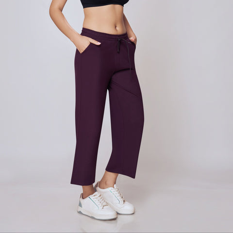 Woman wearing a black sports bra and  Purple Ankle Length Track Pants on a white background