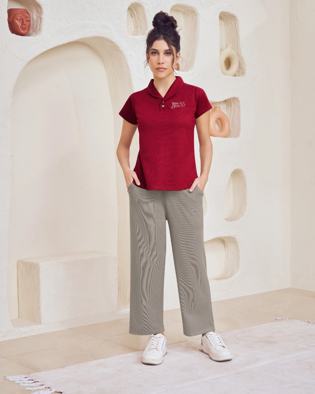 Woman wearing a red polo shirt and gray pants standing in a room with decorative wall art.