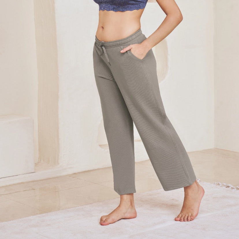 Woman wearing a blue sports bra and gray sweatpants in a minimalistic room.