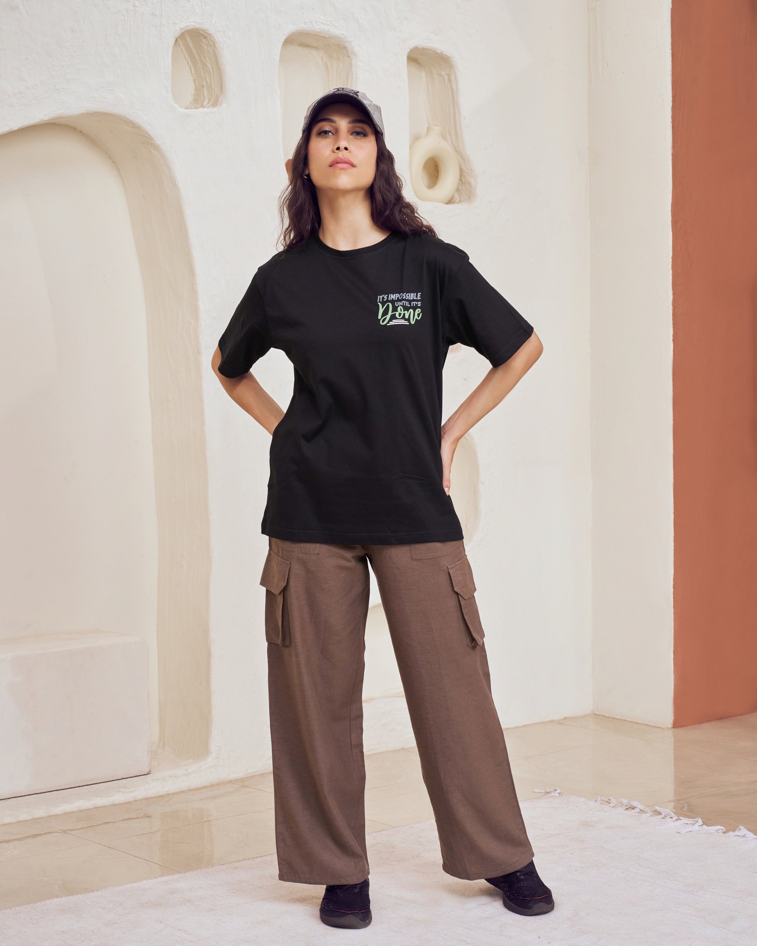 Person wearing a black t-shirt and brown cargo pants standing in a modern indoor setting.