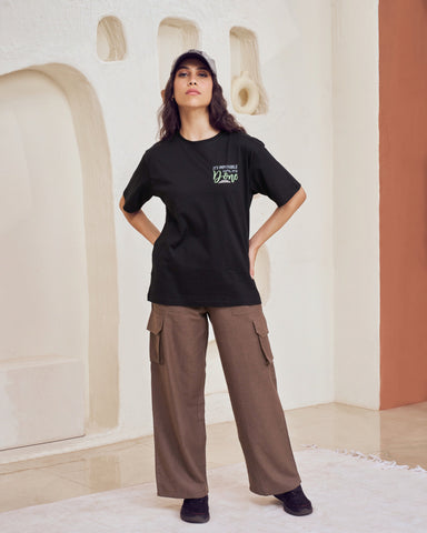 Person wearing a black t-shirt and brown cargo pants standing in a modern indoor setting.