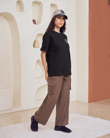 Person wearing a black t-shirt and brown pants standing in a modern architectural setting.