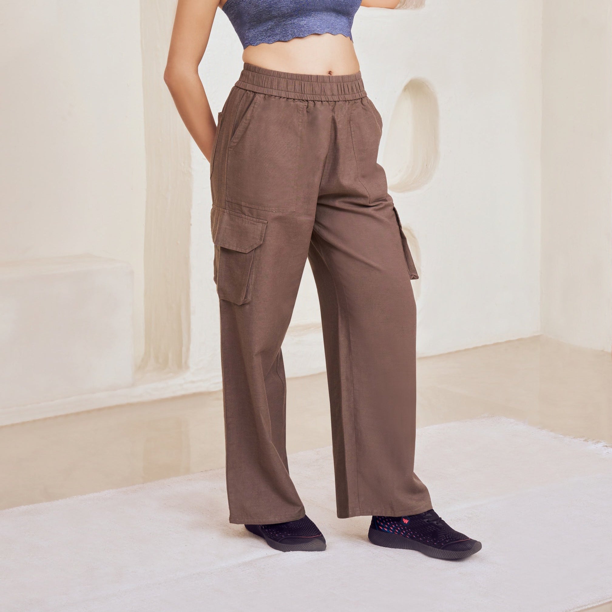 Woman wearing a blue top and brown pants standing in a room with textured walls.