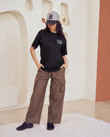 Person wearing a black t-shirt with a logo and brown cargo pants in a modern indoor setting.