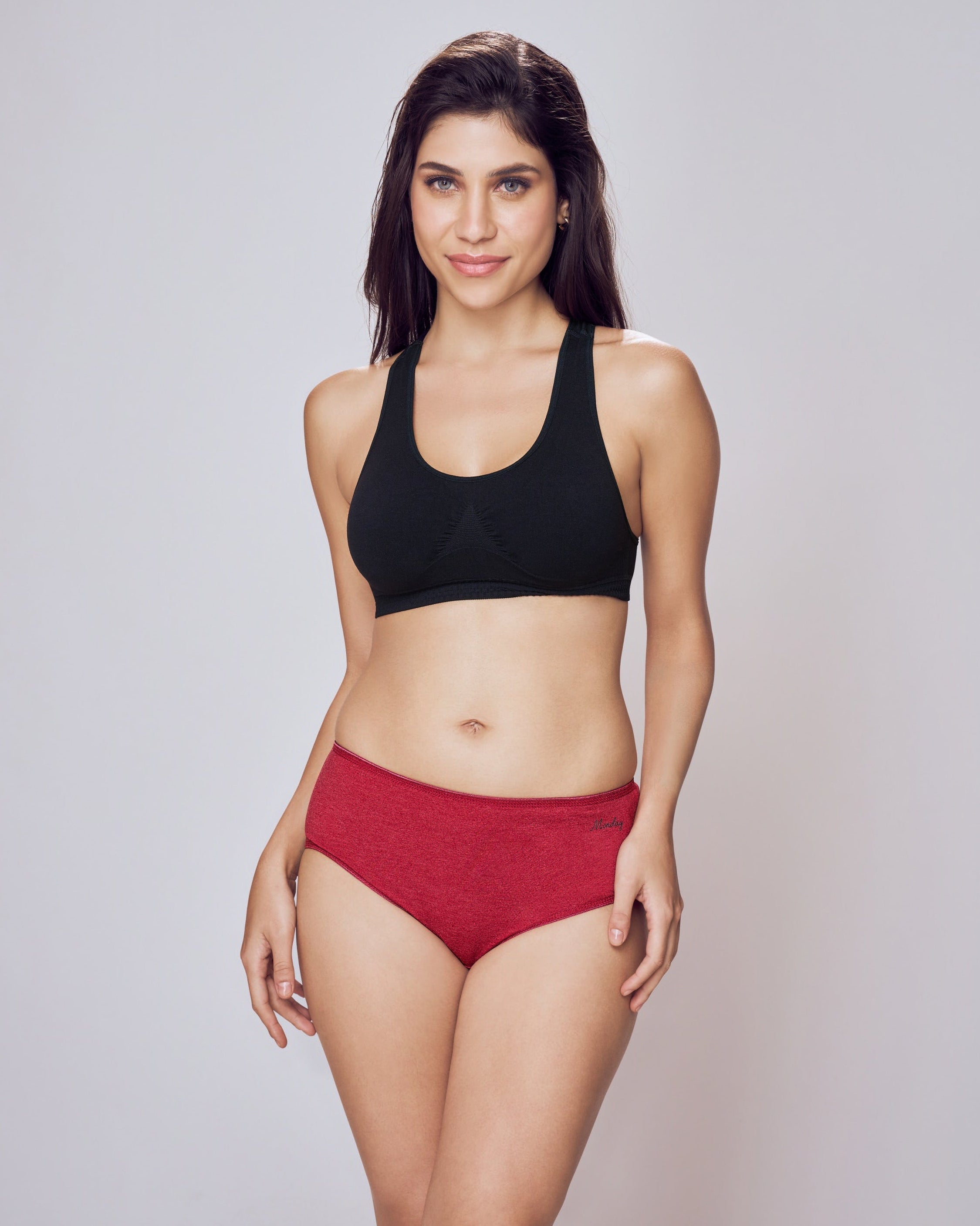 Woman wearing a black sports bra and red high-waisted bikini bottoms on a plain background