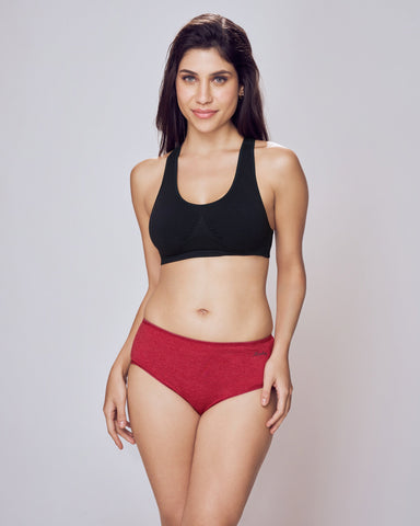 Woman wearing a black sports bra and red high-waisted bikini bottoms on a plain background